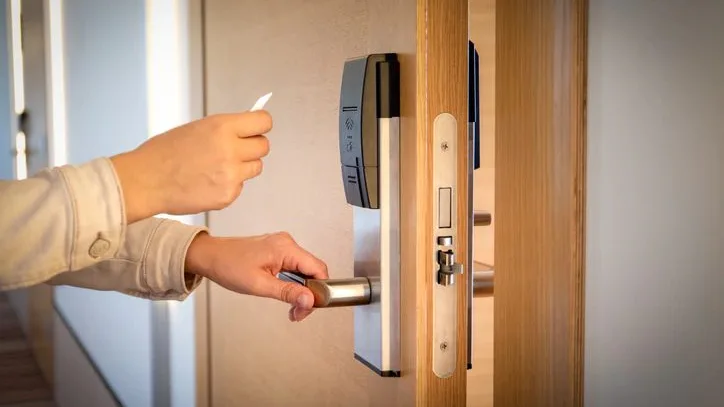 Hand using a hotel key card to unlock a door, illustrating the top FAQs about hotel key cards and their functionality.